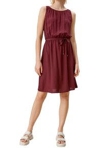 Vestido burdeos sin mangas con escote fruncido y cintura con cordón, que presenta una silueta fluida y una tela suave. Combinado con sandalias ligeras.