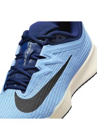 Svijetloplave i tamnoplave sportske tenisice s crnim Nike swooshom, zigzag preklopom i natpisom "Vapor Pro" na jeziku, prikazujući prednje i bočne detalje.