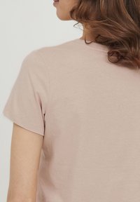 Camiseta de manga corta, de color rosa claro, con una textura suave y un cuello redondo; presenta costuras mínimas y un ajuste relajado.