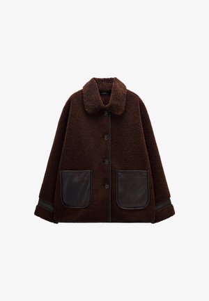 Brązowa kurtka z polaru z zapięciem na guziki, dużymi skórzanymi kieszeniami, kołnierzem i kontrastowymi skórzanymi akcentami na rękawach. Miękka tekstura.