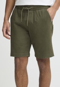 Alyvuogių žalios spalvos šortai iš minkštos medžiagos, su raišteliu juosmens srityje, šoninėmis kišenėmis ir siūtomis apačiomis, užtikrinančiomis didesnį patvarumą.