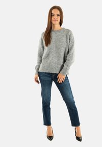 Suéter de punto gris claro con puños y dobladillo acanalados, combinado con jeans azul y tacones negros de punta. La tela parece suave y texturizada.