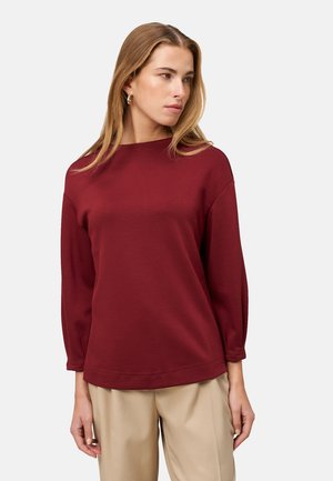 Bordeaux sweatshirt met een ronde halslijn, wijde mouwen en een relaxte pasvorm, gemaakt van zachte stof; gecombineerd met beige broeken.