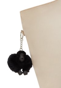 Beige tote bag with a textured finish, featuring a black gorilla keychain with a fuzzy body and smooth face, attached with a metal ring.