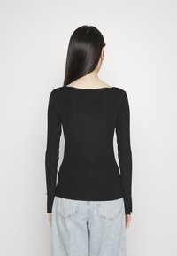 Czarny top z długim rękawem wykonany z prążkowanego materiału, z wycięciem na plecach w kształcie litery U, dopasowany fason z subtelnymi rozcięciami po bokach na dole.