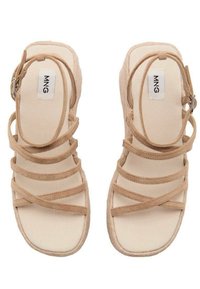 Beige snörsandaler med en texturerad ovandel och platt sula. Har flera korsande remmar och en justerbar ankelspänne.
