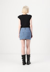 Svart kortermet topp kombinert med et lys blått denim mini-skjørt. Svart knehøye støvler med flere sølvspenne. En enkel hvit bakgrunn.