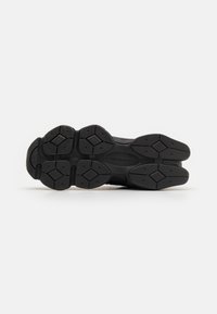Semelle de chaussure de sport noire avec un motif texturé, comportant des sections en caoutchouc surélevées et des accents en forme de losange pour l'adhérence.