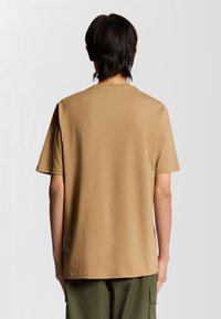 Khaki bomull t-shirt med korta ärmar och rund halsringning. Slät textur och avslappnad passform, visad från baksidan.