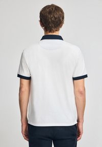 Hvid polo-shirt med navyblå krave og ærmekant, med et klassisk fit og en glat tekstur, vist fra ryggen.