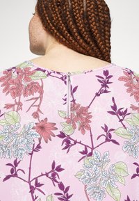 Látka s fialovými a růžovými květinovými vzory se zipem na zadní straně. Hladká textura a design s krátkými rukávy.