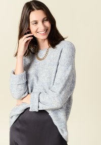 Maglione azzurro chiaro a maglia con una vestibilità comoda e polsini arrotolati. Abbinato a una gonna scura, con una collana di catena dorata spessa.