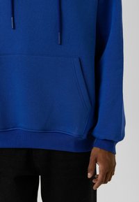 Blauwe pullover hoodie met een grote voorkant zak, verstelbare trekkoorden en ribgebreide cuffs. Gemaakt van zachte stof met een gladde textuur.