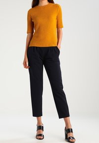 Maglietta a maniche corte a coste color senape con scollatura rotonda, abbinata a pantaloni tapered blu navy e sandali con tacco a blocco neri.