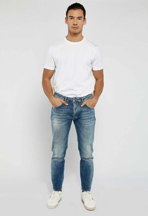 Fitted blue jeans with fading and whiskering, paired with a plain white short-sleeve t-shirt, worn with white sneakers.
