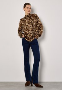 Bluzka w panterkę z wysokim dekoltem i długimi rękawami, zestawiona z ciemnoniebieskimi dżinsami w kształcie dzwonów z bocznym rozcięciem oraz brązowymi botkami za kostkę.