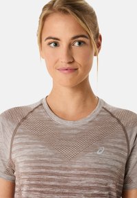 Koszulka sportowa z krótkim rękawem, cechująca się teksturowanym wzorem w odcieniach beżu, z geometrycznym motywem oraz detalem logo na lewej piersi.