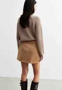 Beige gerippten Pullover kombiniert mit einem beigen Wildleder-Minirock, der eine ausgestellte Form und saubere Nähte aufweist, ergänzt durch schwarze knielange Stiefel.