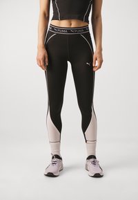 Czarne legginsy sportowe z jasnoróżowymi akcentami, z wysokim stanem i wygiętymi panelami. Noszone z różowymi sneakersami i białymi skarpetkami.