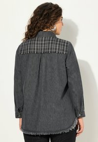 Charcoal-graues Hemd mit kariertem Yoke-Design, ausgefranstem Saum, geknöpften Manschetten und langen Ärmeln. Hergestellt aus weichem Denim-Stoff.
