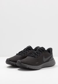 Une paire de chaussures de running Nike noires en tissu maillé texturé, avec des semelles rembourrées et des lacets, sur une surface blanche.