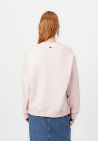Felpa rosa con scollo rotondo e polsini a coste. Presenta un piccolo logo verde sul retro. Abbinata a una gonna di jeans.