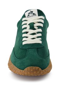 Baskets en suède vert avec des lacets blancs, semelle marron texturée et logo "le coq sportif" sur la languette, vues de l'avant.