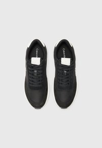 Zwarte sneakers met een mix van gladde en gestructureerde materialen, voorzien van een witte zool en subtiele branding op de tong en zijkant.
