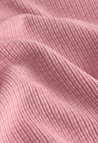 Tissu rose texturé avec nervures verticales, créant un aspect doux et légèrement ondulé ; le matériau semble moelleux et tactile.