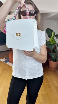 Sac à main blanc avec quincaillerie dorée, anse à motif floral, design structuré, texture lisse, avec un rabat triangulaire et un fermoir carré.