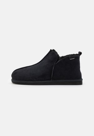 Chaussons en daim noir à enfiler, avec une doublure intérieure douce et duveteuse et un bout rond. Semelle en caoutchouc noir durable et détails de couture sur le côté.