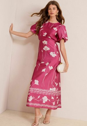 Robe maxi florale rose avec des manches bouffantes et une taille cintrée. Elle présente des motifs floraux blancs et des borduresintriquées à l'ourlet.