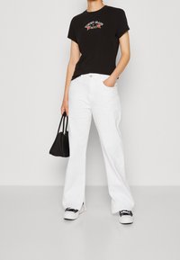 Černé bavlněné tričko s vyšívaným nápisem "Tommy Jeans NYC" v barvě, spárované s volnými bílými džínami a černou kabelkou. Bílé tenisky.