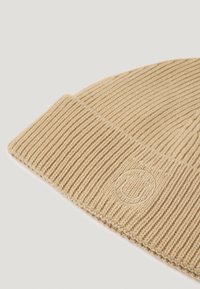 Căciulă tricotată de culoare bej deschis, cu o textură ribbată și un logo subtil brodat cu un zâmbet în față. Material moale și flexibil.