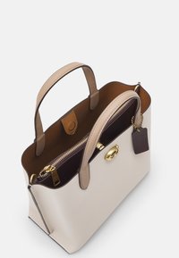 Strukturalna torba na ramię w kremowej teksturowanej skórze, z brązowymi skórzanymi uchwytami, złotymi akcesoriami oraz zamykaną na zamek wnętrzem o ciemnym wykończeniu.