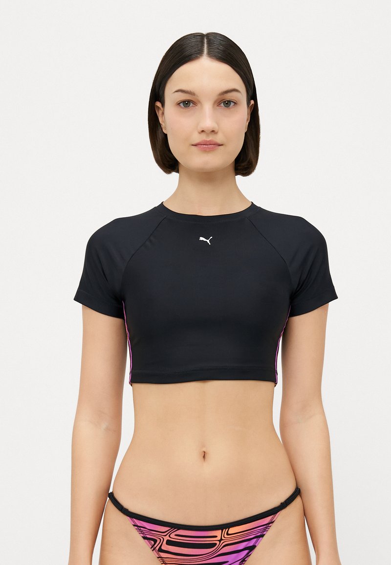 Μαύρο κοντό αθλητικό τοπ με στρογγυλή λαιμόκοψη, κοντά μανίκια και ροζ λεπτομέρειες στο πλάι. Διαθέτει ένα μικρό λευκό λογότυπο Puma στο στήθος.