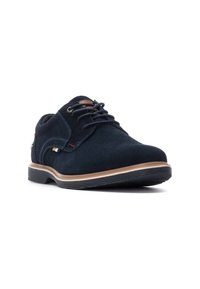 Zapato de ante azul marino con punta redonda, diseño con cordones, suela de color marrón claro en contraste y sutiles acentos en rojo y amarillo en el lateral.
