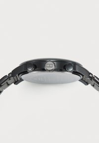 Montre en acier inoxydable noir avec un boîtier rond, deux boutons latéraux et une texture métallique brossée. Surface lisse avec un design minimaliste.
