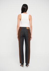 Braune und schwarze Jeans mit geradem Schnitt, die ein kontrastierendes Seitenpaneeldesign und ein Markenlabel am Rückenbund aufweisen.