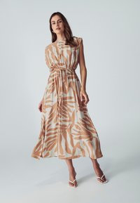 Abito lungo in tessuto leggero con strisce a zebra arancioni e crema. Vita arricciata con dettagli in cordoncino. Design senza maniche, gonna a piena lunghezza.