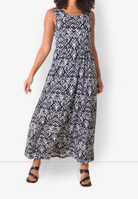 Maxi šaty v černé a bílé barvě s geometrickým vzorem, bez rukávů, s nařaseným pasem, z lehké látky, doplněné černými sandály na tenké pásky.