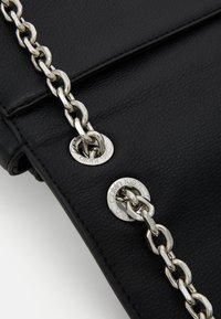 Black leather handbag featuring a silver chain strap and metal hardware with "Calvin Klein" branding on circular accents.