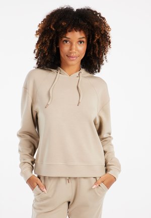 Beige hoodie met een voorkiepocket, verstelbare koordjes en geribbelde manchetten. Soepele textuur met een ontspannen pasvorm, gedragen met bijpassende broek.