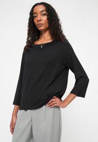 Zwarte top met lange mouwen, een gedrapeerde halslijn en een losse fit, gecombineerd met lichtgrijze gestreepte broeken. Zachte stof met een gladde textuur.