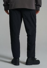 Czarne, teksturowane spodnie o tapered designie. Wykonane z lekkiego materiału, z delikatnymi szwami, w połączeniu z czarnym obuwiem.