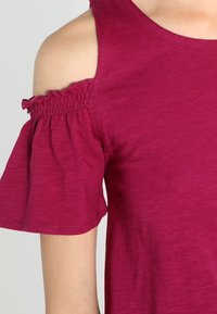 Top de manga corta en color magenta hecho de tela suave, presenta un diseño de hombros descubiertos con detalles fruncidos en las mangas.