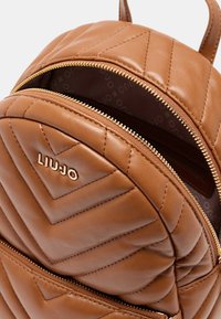 Zaino in pelle trapuntata marrone con cerniera dorata, con un logo ben visibile. Interno foderato in tessuto marrone, che mette in risalto il suo design strutturato.