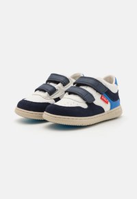 Baskets basses bleu marine et blanches avec des accents bleus, en cuir et en daim, dotées de deux bandes Velcro et d'une semelle en caoutchouc texturé.