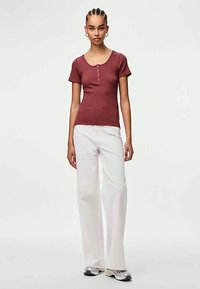 Ribota vīna sarkanā īsām piedurknēm blūze ar apaļu izgriezumu un trim pogām, kombinēta ar baltām platām biksēm un pelēkiem sporta apaviem.