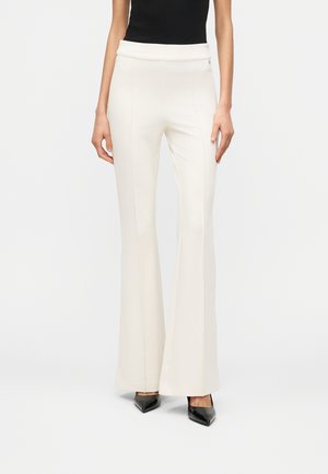 Kvinde iført højtaljede, off-white flared bukser kombineret med sorte spidse hæle og en sort ærmeløs top.